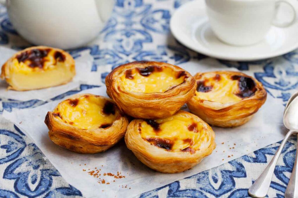 several pastel de nata sitting on a colorful blue and white table with coffee cups