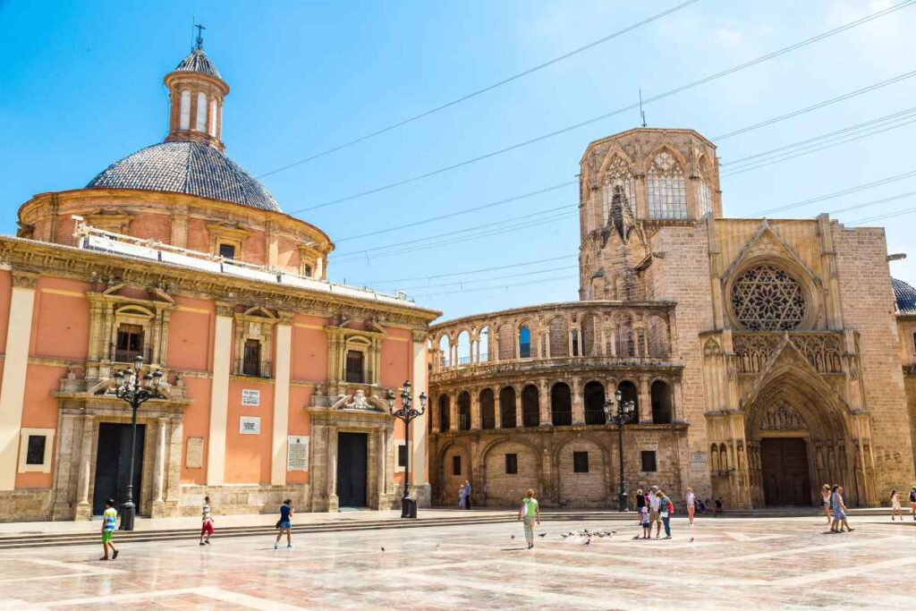 valencia cathedral made of tan stone and peach colored building on Plaça de la Verge in valencia, spain