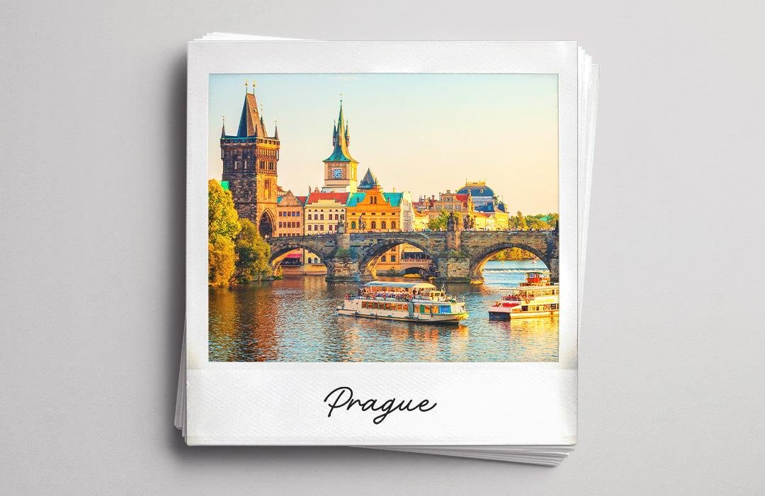A polaroid photo of Prague with the Charles Bridge and a river boat at sunset.
